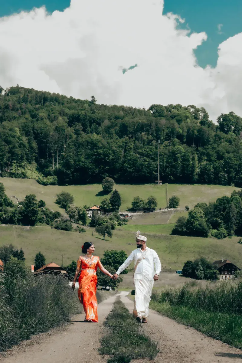A couple walking hand in hand down a country road, hills behind them.